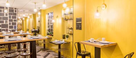 A restaurant with yellow walls, multiple tables with chairs, and hanging light fixtures.