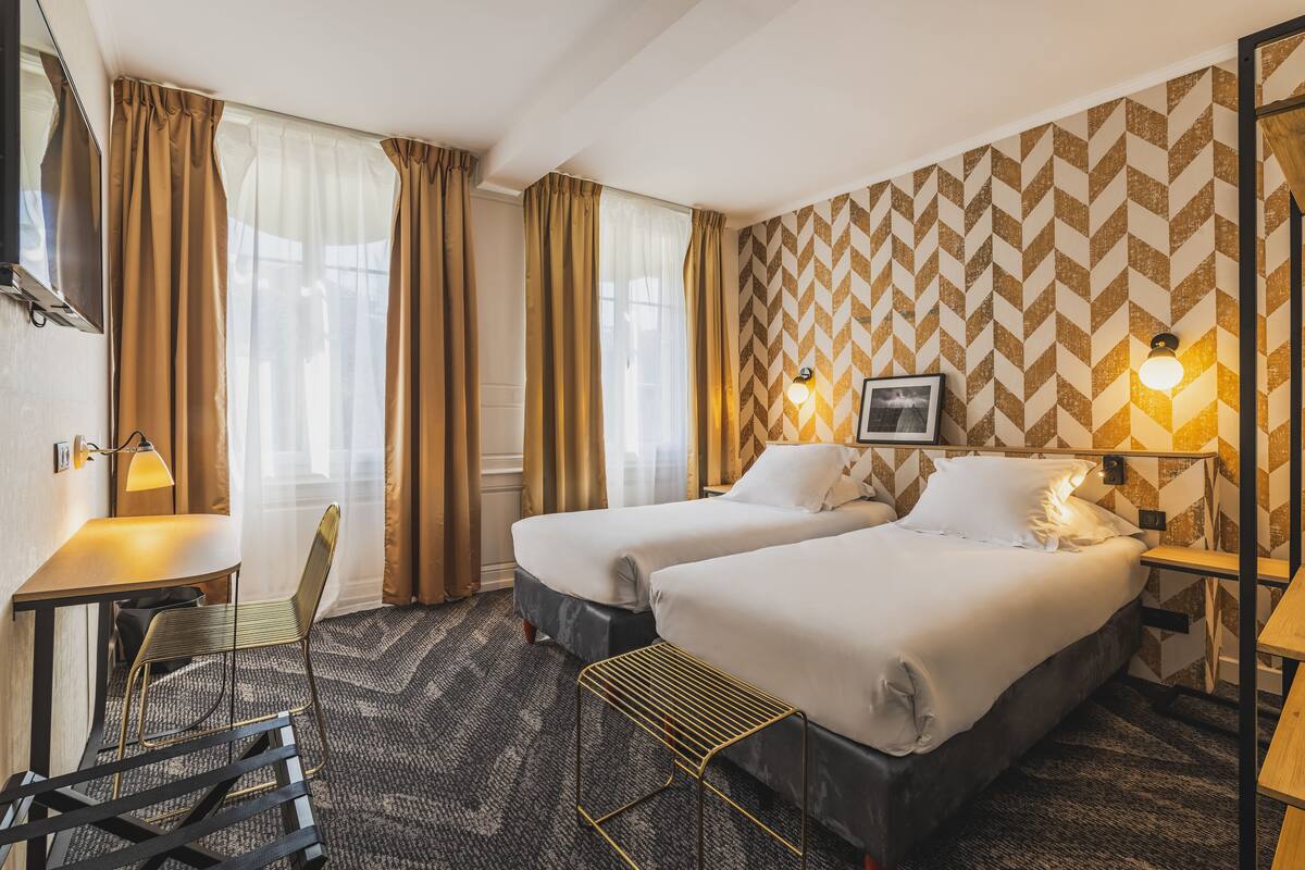 Hotellihuone, jossa on kaksi sänkyä, työpöytä, tuoli ja kuviollinen seinä.