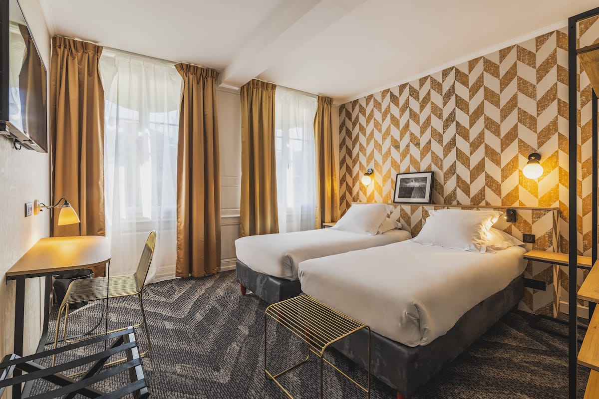 Habitación de hotel con dos camas, un escritorio, una silla y un papel tapiz estampado.