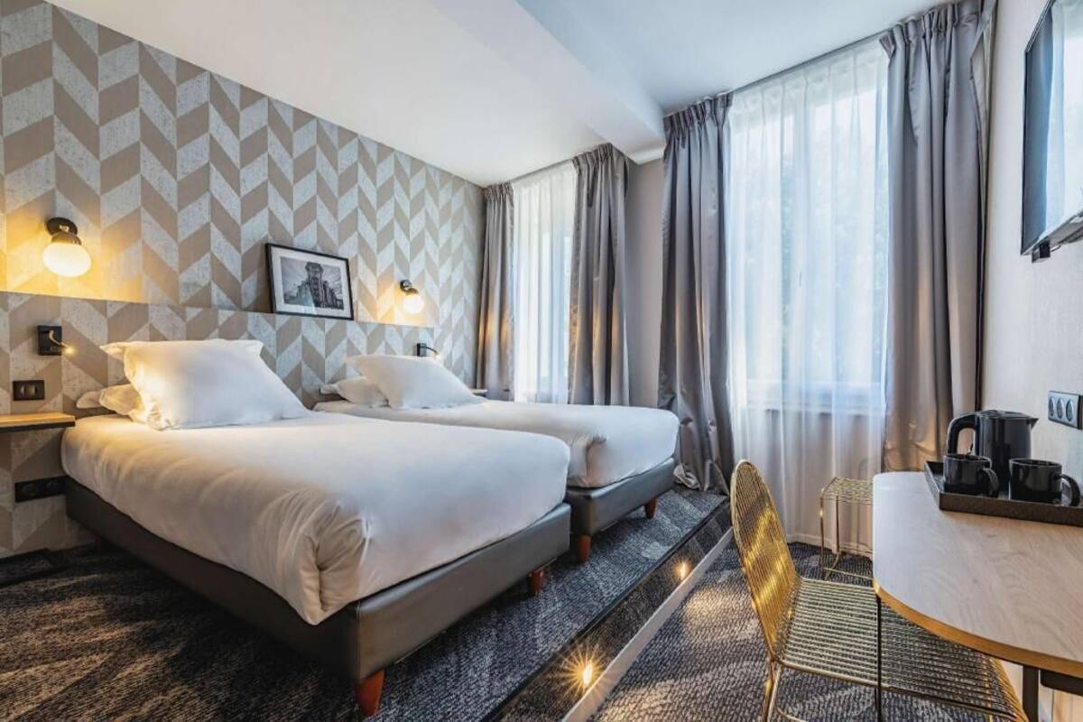 Hotellihuone, jossa on kaksi sänkyä, työpöytä, tuoli ja taulu seinällä.