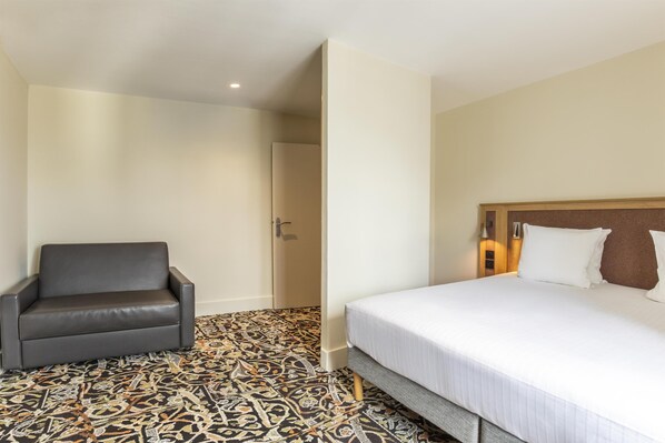 A hotel room with a bed, a chair, and a patterned floor.