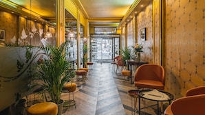 Et hotel lobby med fiskebensmønstret gulv, siddeområder og dekorative planter.