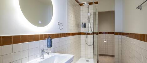 A bathroom with a sink, mirror, shower, and tiled walls.