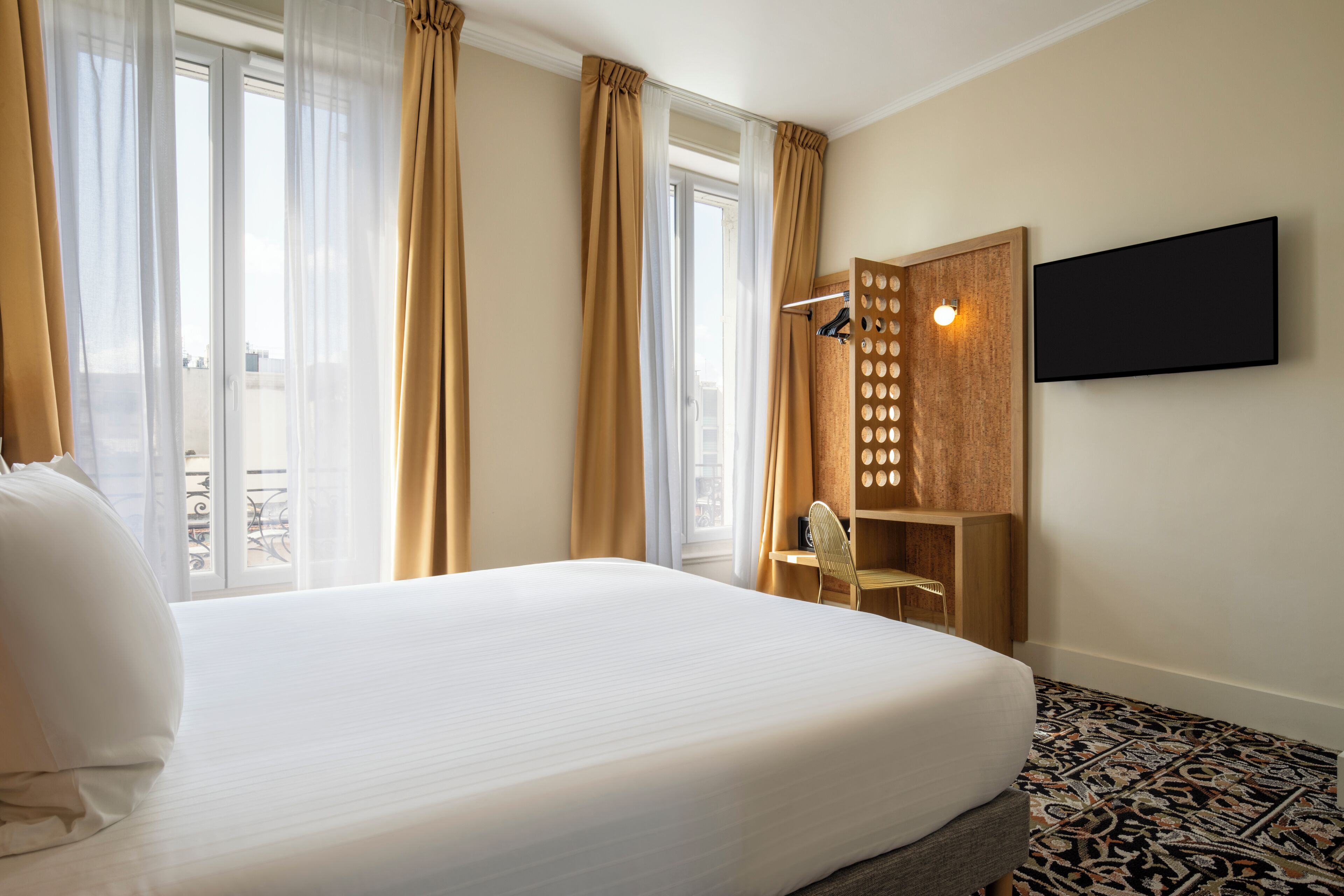 Une chambre d’hôtel avec un grand lit, un téléviseur fixé au mur et une fenêtre avec des rideaux.