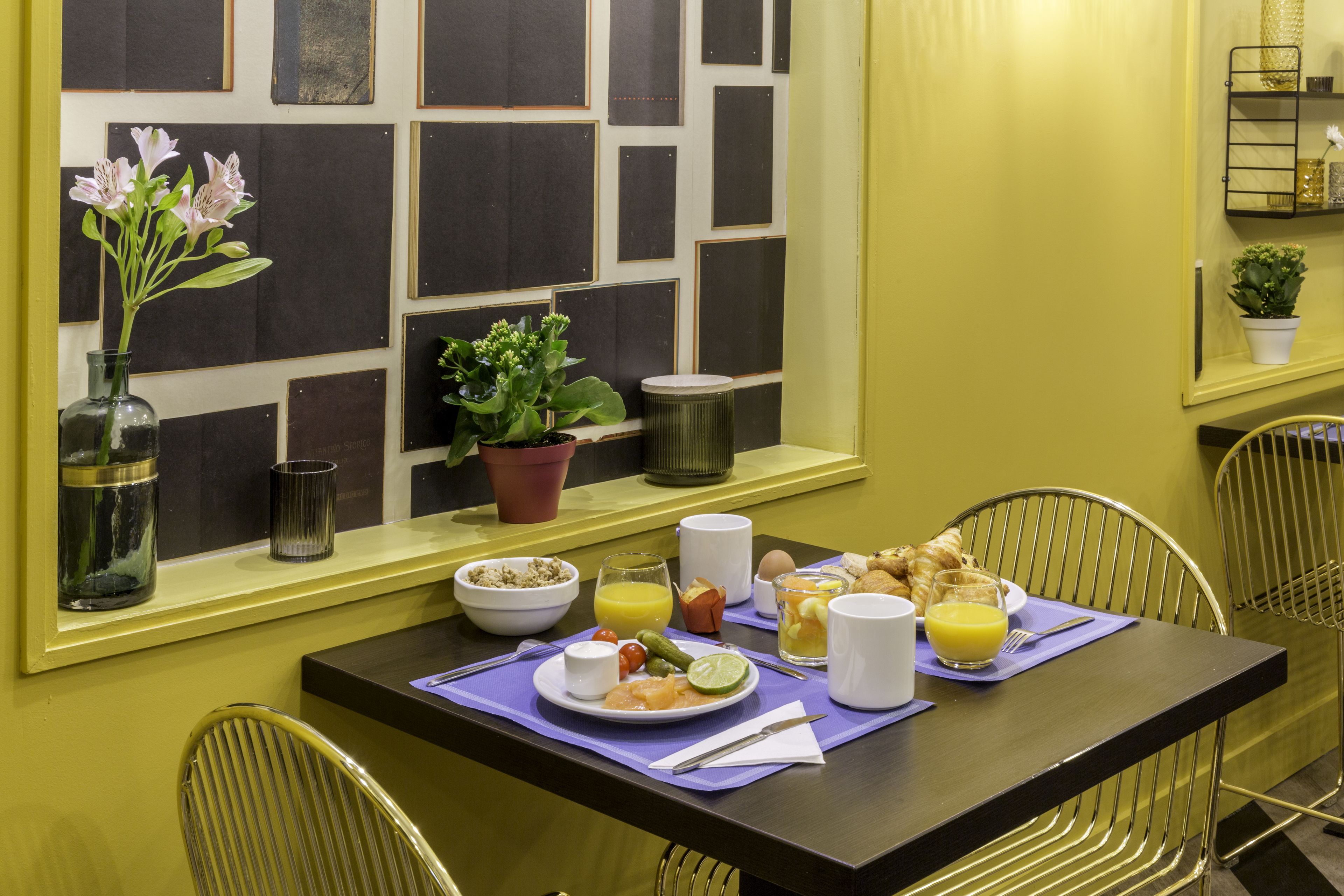 A breakfast table set with plates, cutlery, and a vase of flowers.