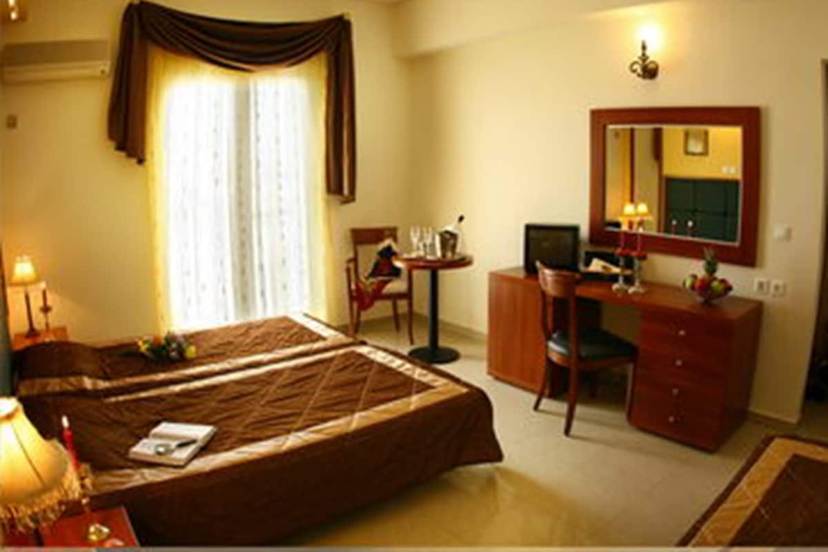 A hotel room with a bed, a desk, a chair, a dresser, a mirror, and a window with curtains.