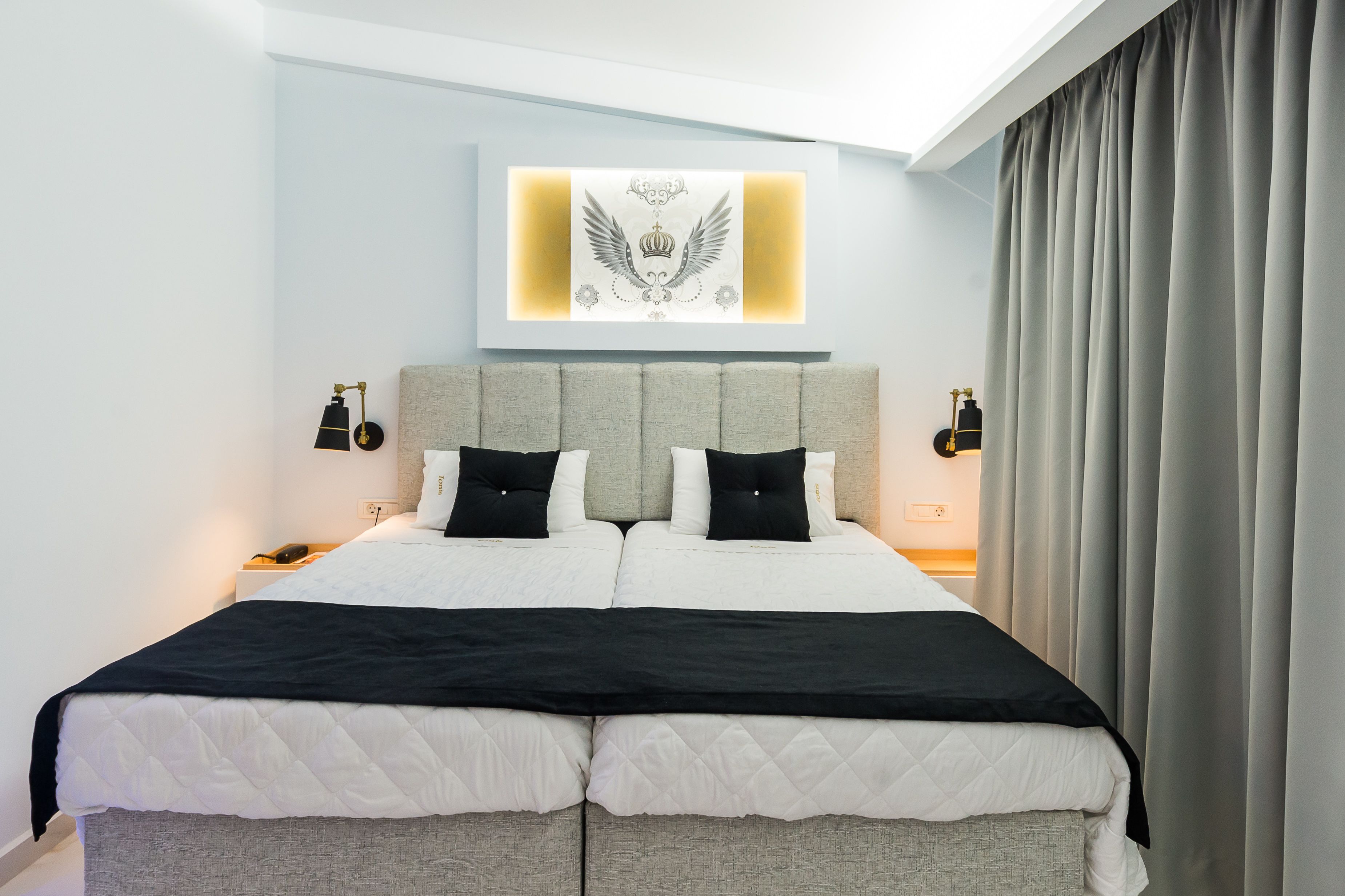 A modern hotel room with a large bed, grey headboard, and a wall-mounted artwork.