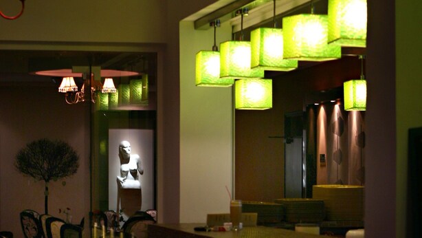 A dimly lit bar area with patterned tablecloths, chairs, and green hanging lamps. - Ionis Art Hotel (Zakynthos)
