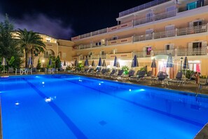 A swimming pool with lounge chairs and umbrellas, surrounded by a multi-story building with balconies. - Ionis Art Hotel (Zakynthos)