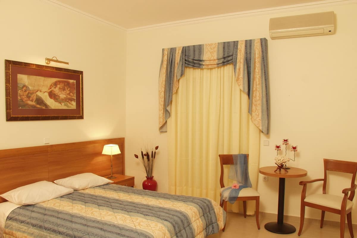 A hotel room with a bed, a nightstand, a lamp, a chair, a table with a vase, and a painting on the wall.