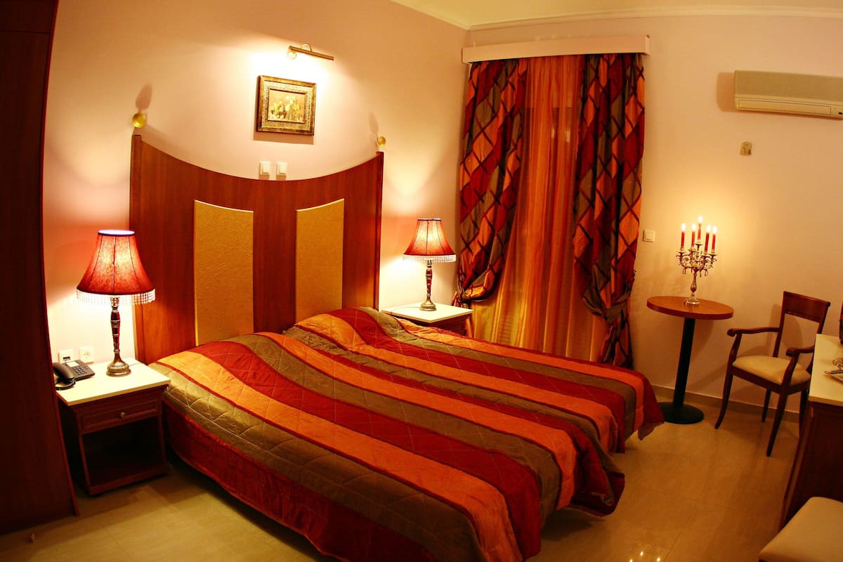 A hotel room with a large bed, two bedside tables with lamps, a small round table with a candelabra, a chair, and a desk with a chair.