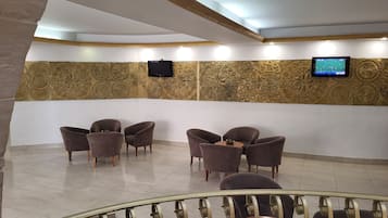 En lobby med tapetvæg, et fladskærms-tv og flere siddeområder med stole og et lille bord.