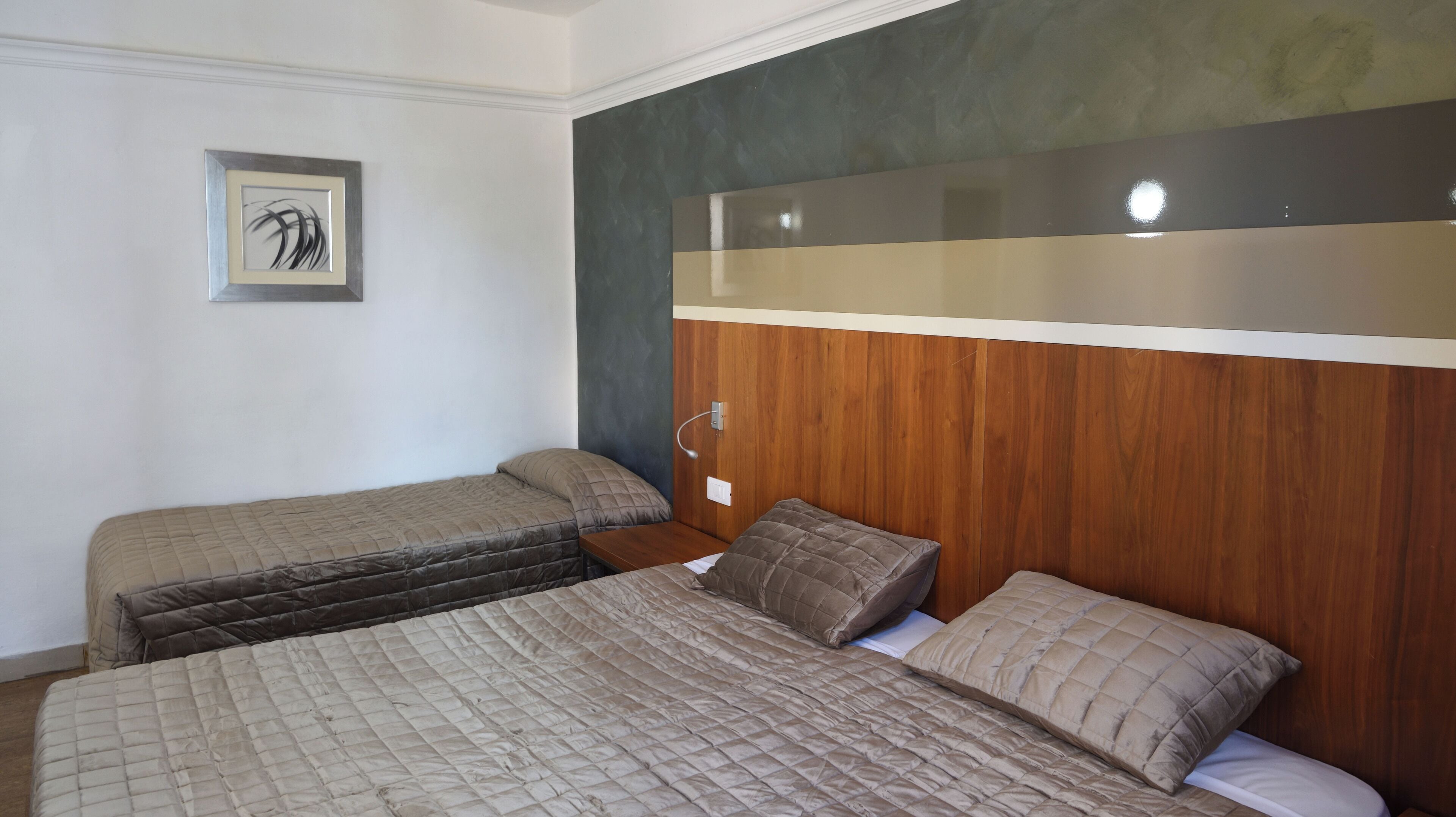 A hotel room with two beds, wooden headboard, a framed picture on the wall, and a bedside table with a lamp.