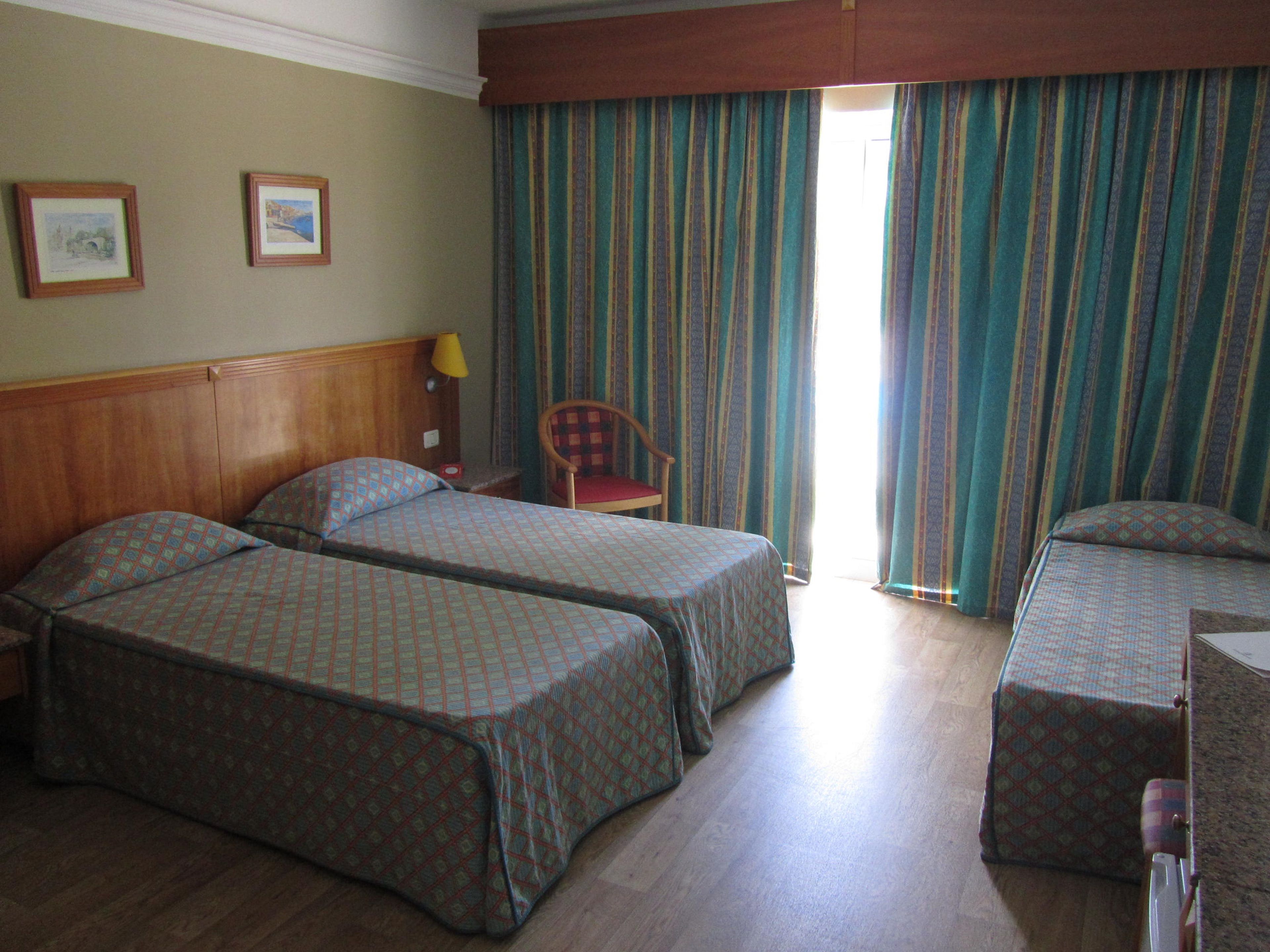 A hotel room with two beds, a chair, a desk, and a window with curtains.