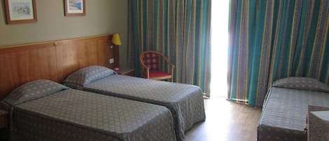 A hotel room with two beds, a chair, a desk, and a window with curtains.