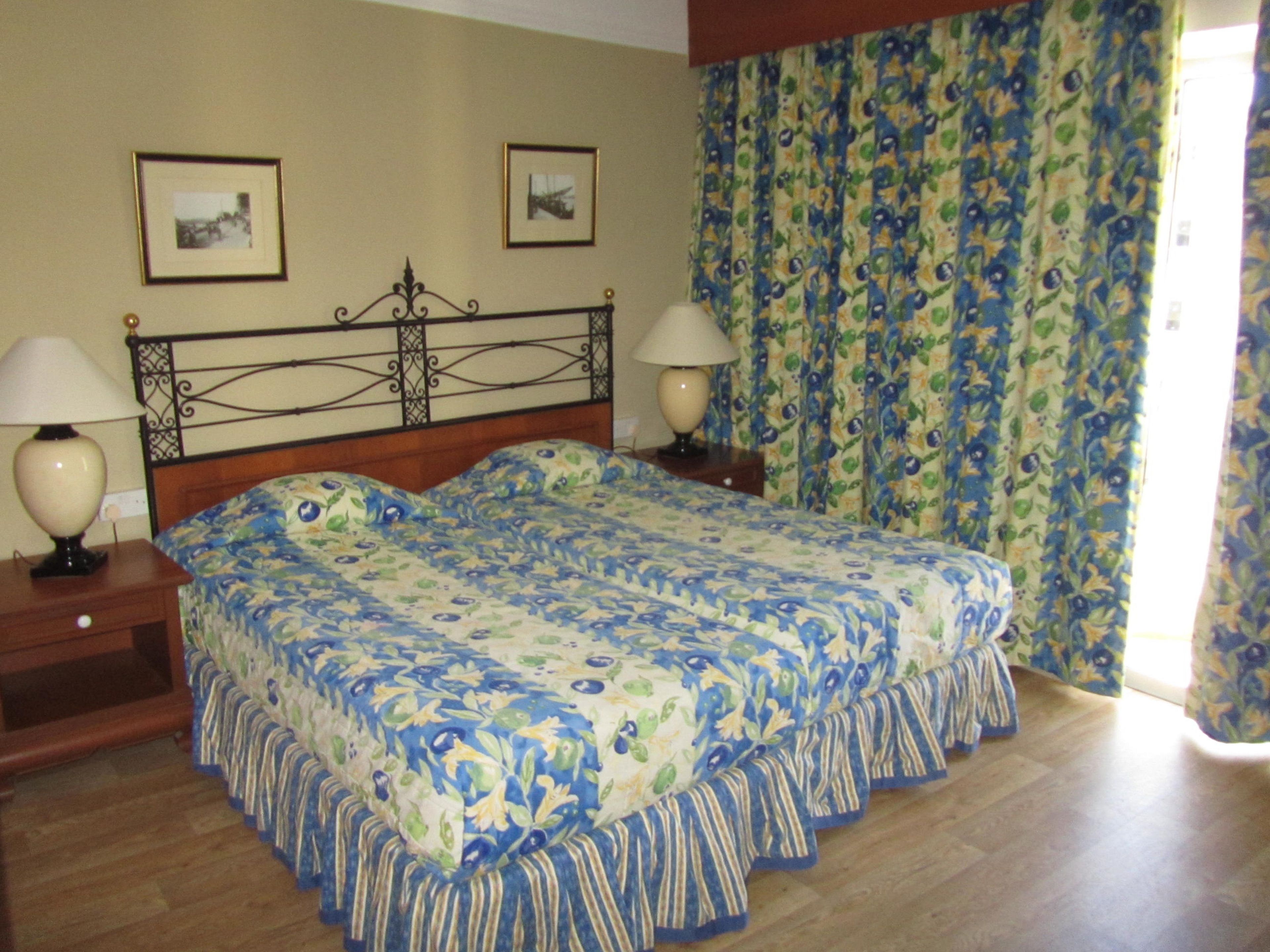 A double bed with floral bedding, two bedside tables with lamps, and a curtain with a fruit pattern.