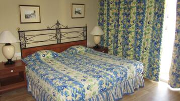 A double bed with floral bedding, two bedside tables with lamps, and a curtain with a fruit pattern.