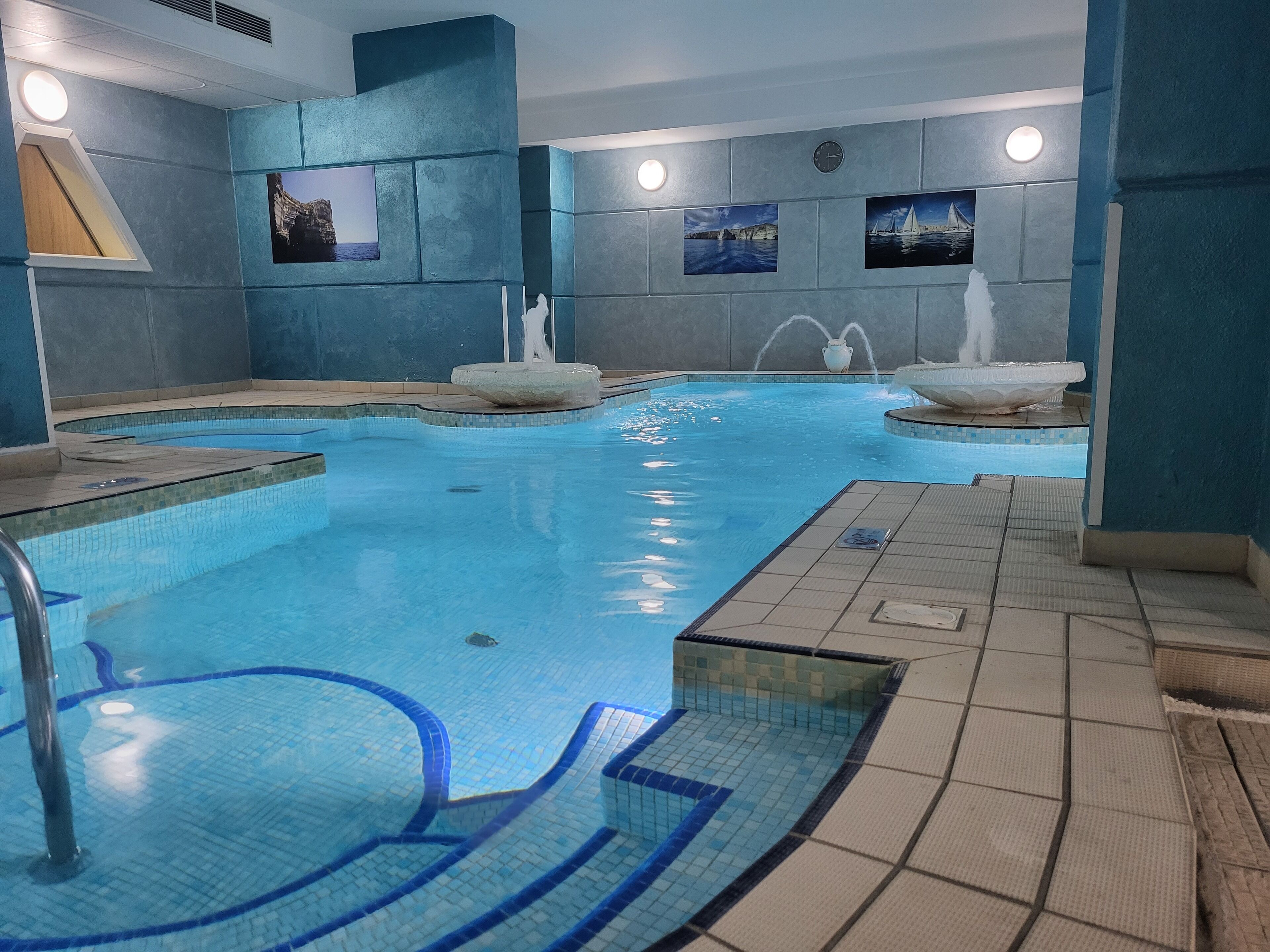 Una piscina interior con múltiples carriles, una fuente central y detalles decorativos en las paredes.