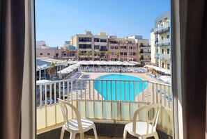 A balcony with a pool, lounge chairs, and umbrellas. - Topaz Hotel (St. Paul's Bay)