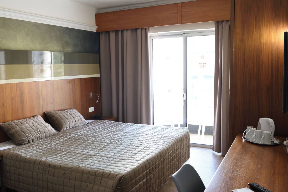 Habitación de hotel con una cama grande, cabecera de madera, escritorio con cafetera y vista al exterior a través de una puerta corrediza.