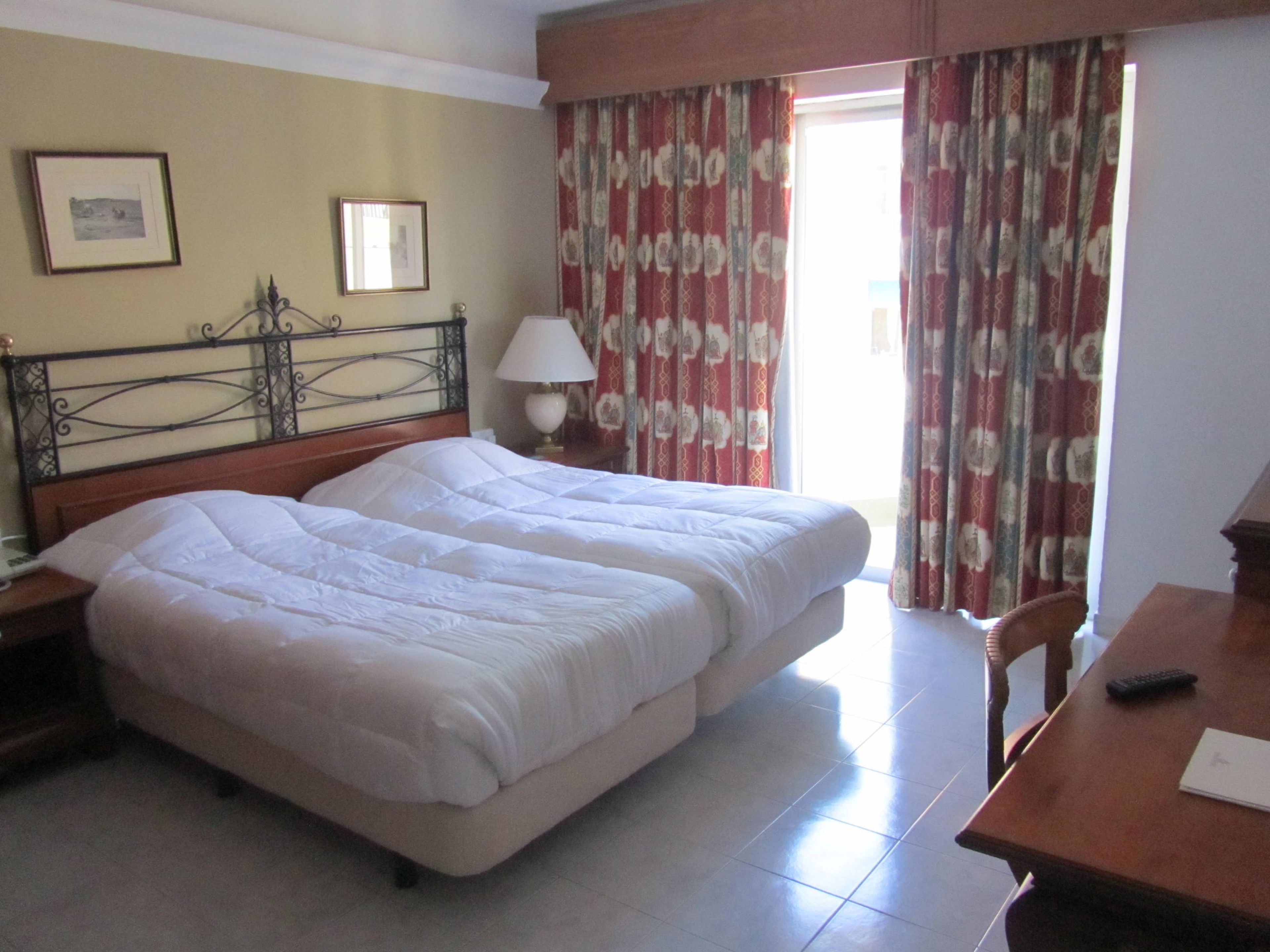 Une chambre d’hôtel avec un lit double, une table de chevet avec une lampe, une chaise, un bureau avec une télécommande et des rideaux.
