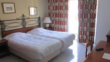 Une chambre d’hôtel avec un lit double, une table de chevet avec une lampe, une chaise, un bureau avec une télécommande et des rideaux.