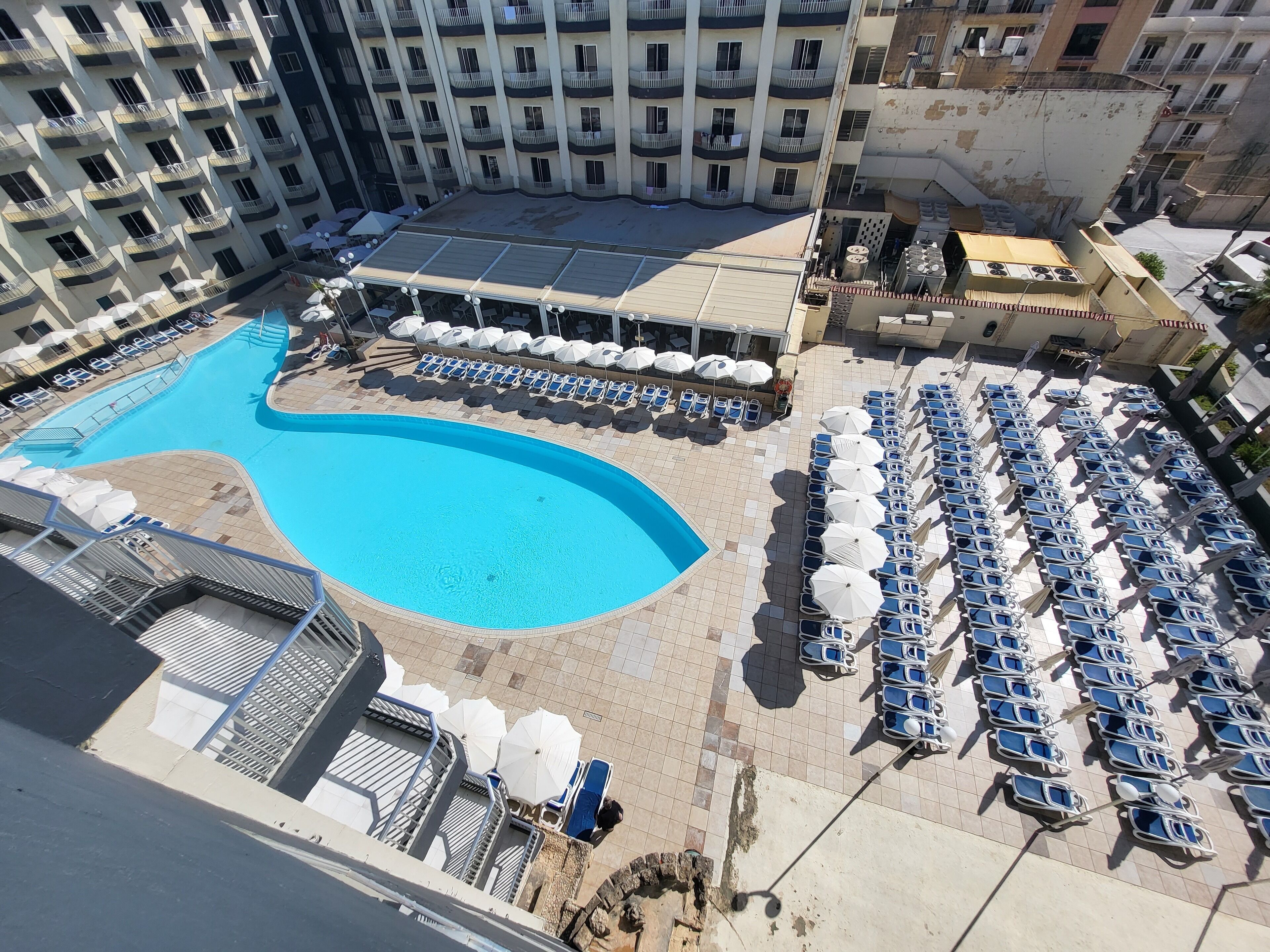 Une piscine entourée de chaises longues et de parasols, avec un bâtiment en arrière-plan.
