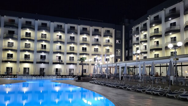 Una piscina con sillones de descanso y sombrillas, rodeada por un edificio con varios balcones y ventanas.