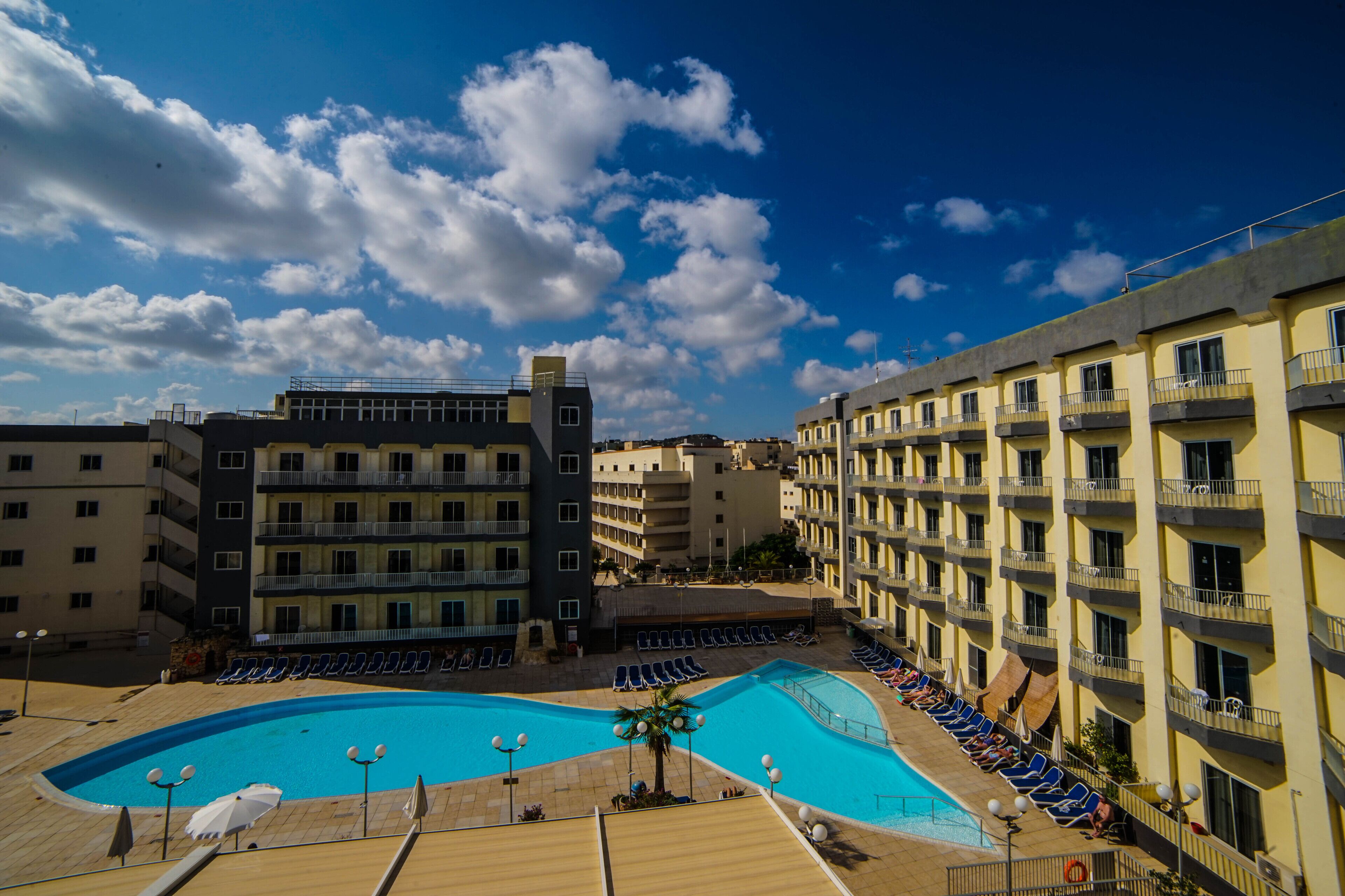 Un hôtel doté d’une piscine entourée de chaises longues, avec un ciel bleu dégagé.