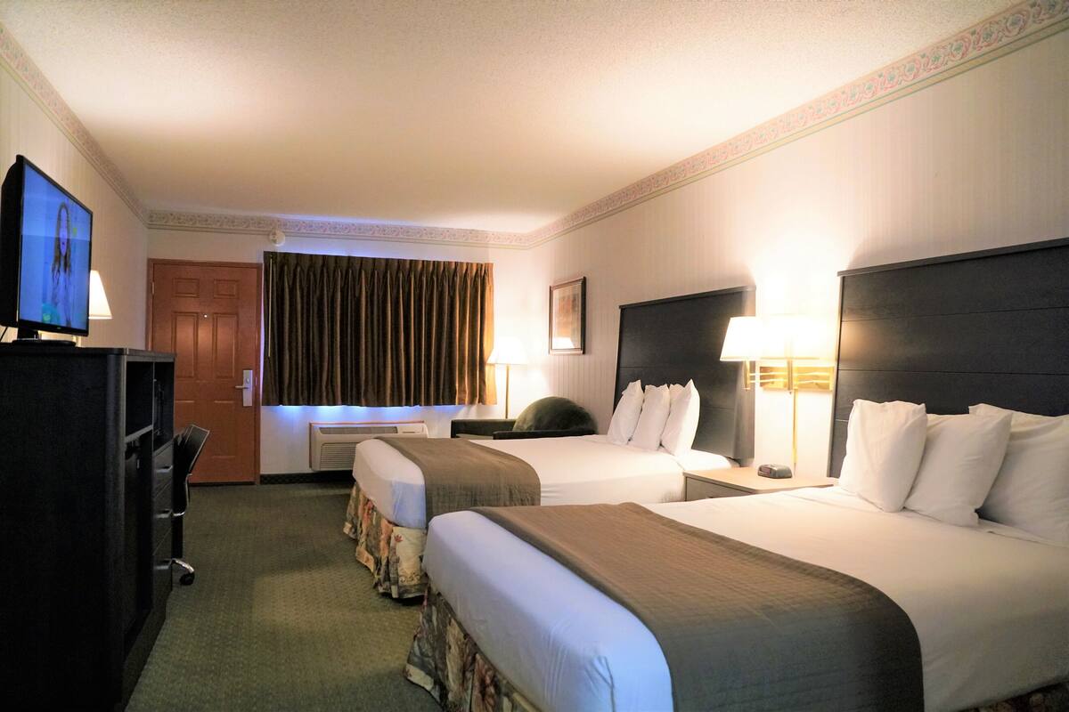 A hotel room with two beds, a TV, a desk, and a lamp.