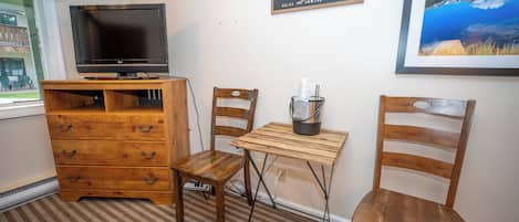 A room with a wooden dresser, a television on top, a small table with a candle, and two wooden chairs.