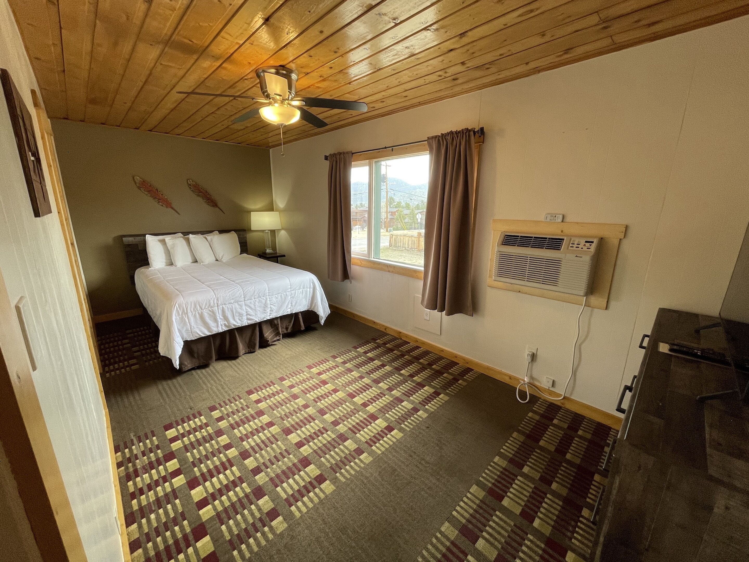 Ein Schlafzimmer mit einem Bett, einem Deckenventilator, einem Fenster mit Vorhängen, einer Klimaanlage und einem gemusterten Teppich.