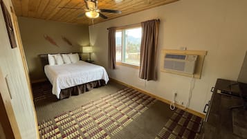 Ein Schlafzimmer mit einem Bett, einem Deckenventilator, einem Fenster mit Vorhängen, einer Klimaanlage und einem gemusterten Teppich.
