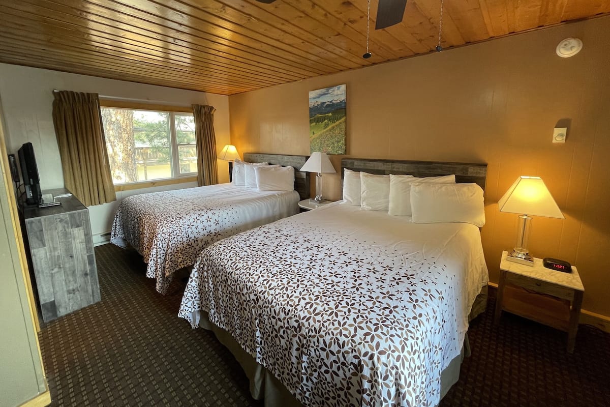 A hotel room with two beds, a desk, a TV, and a painting on the wall.