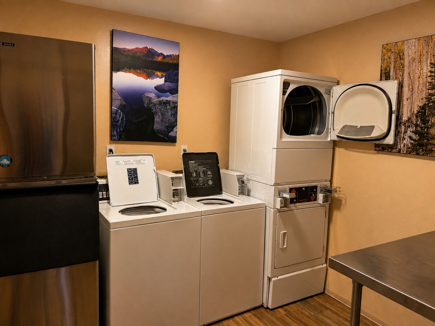 Een kleine wasruimte met een koelkast, een wasmachine, een droger en een wandrek om was op te hangen.