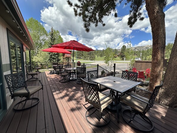 An outdoor patio with wooden tables and chairs, red umbrellas, and a view of a golf course. - Estes Mountain Inn (Estes Park)