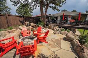 A patio area with red Adirondack chairs, a fire pit, and a stone deck. - Estes Mountain Inn (Estes Park)