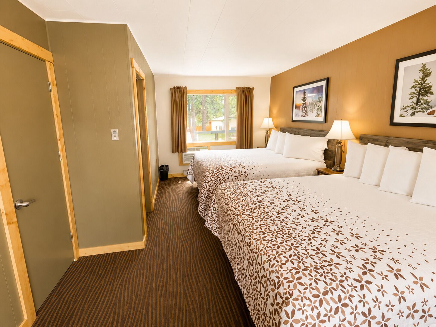 A hotel room with two beds, a window with curtains, a framed picture on the wall, and a door on the left.