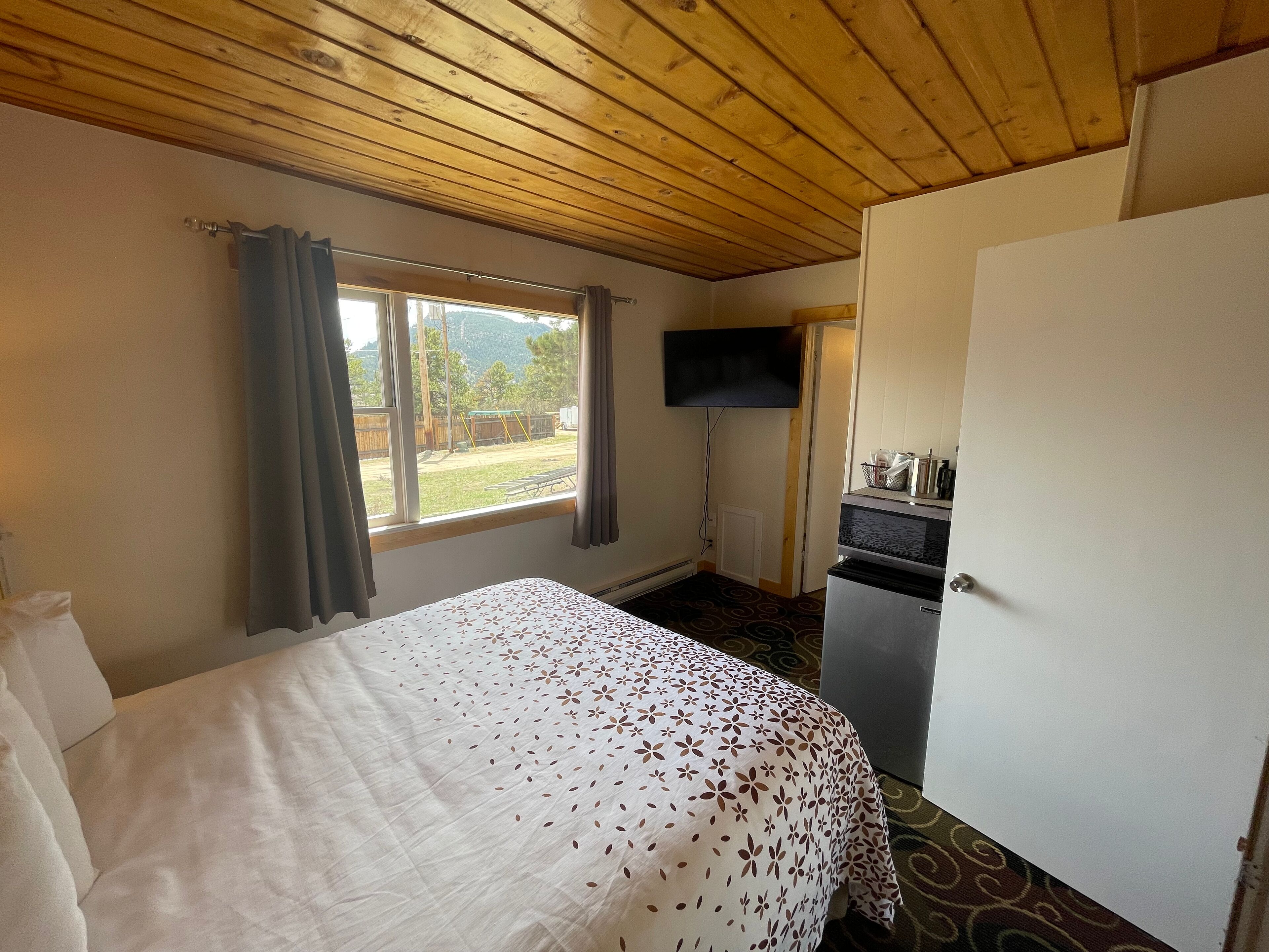 A room with a bed, a television, a small kitchenette, and a window with curtains.