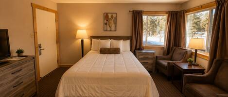 A hotel room with a large bed, a desk, a chair, a television, and a window with curtains.