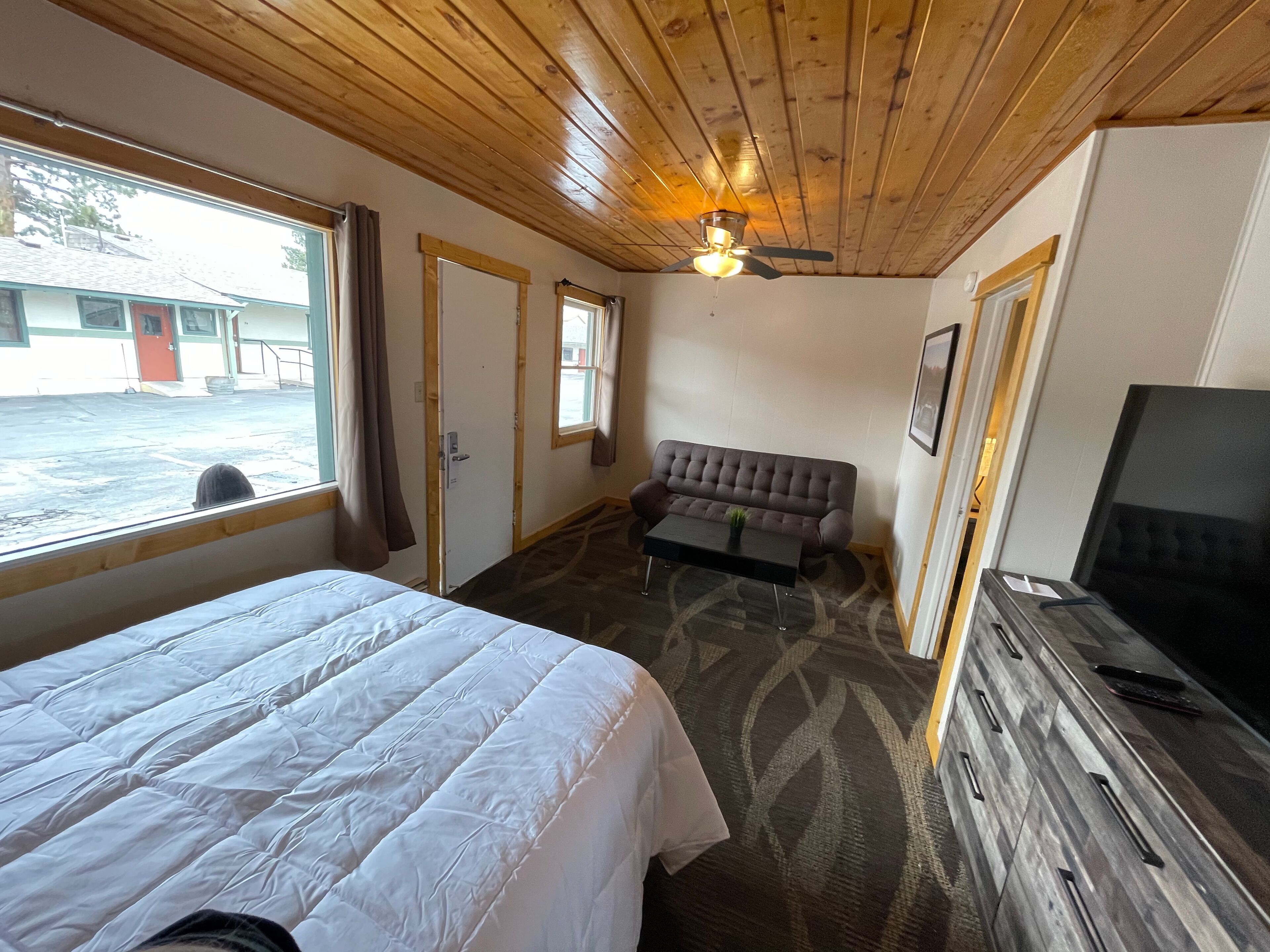 Une chambre d’hôtel avec un lit, un canapé, une télévision et une fenêtre avec des rideaux.