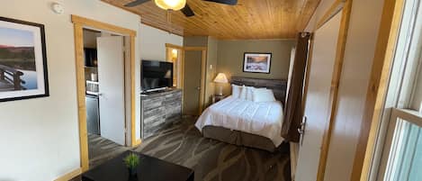 A bedroom with a bed, a desk, a ceiling fan, a TV, and a door leading to a bathroom.
