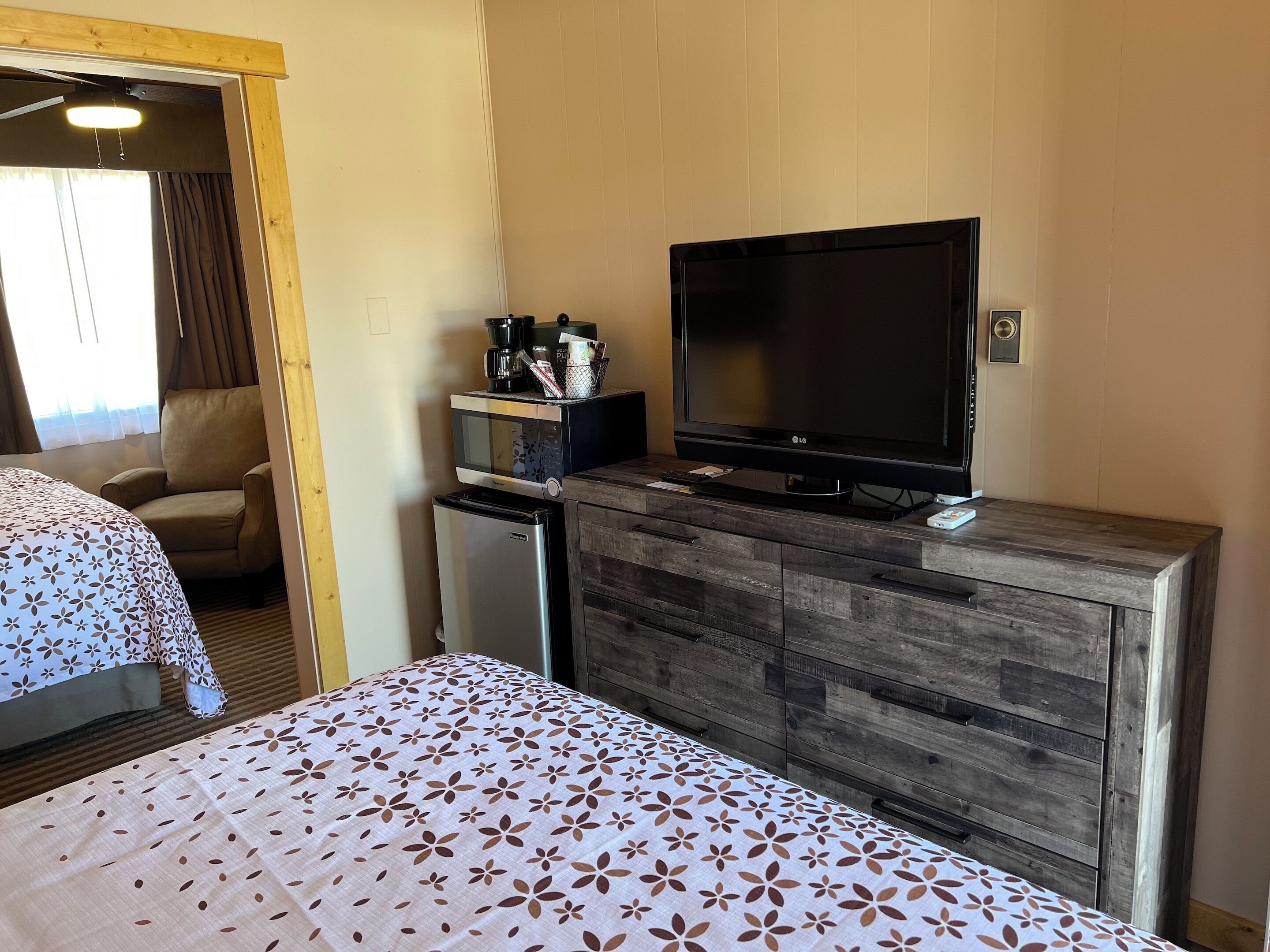 Una habitación de hotel con una cama, un televisor, un refrigerador pequeño y un aparador de madera.