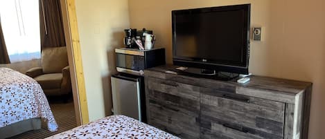 Una habitación de hotel con una cama, un televisor, un refrigerador pequeño y un aparador de madera.