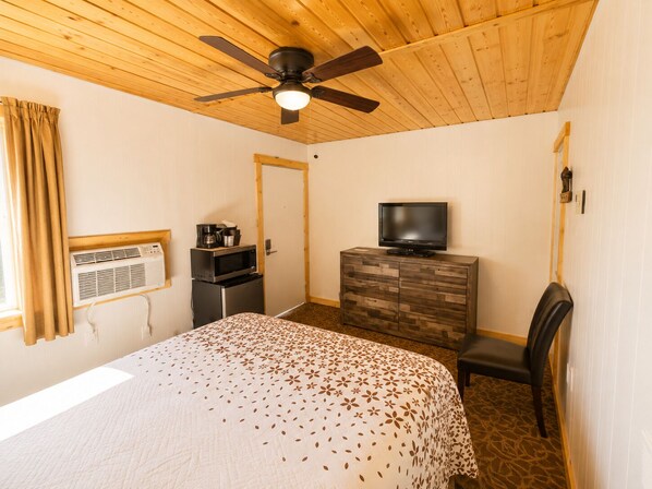 A hotel room with a bed, a television on a wooden dresser, a ceiling fan, and a window with curtains. - Estes Mountain Inn (Estes Park)