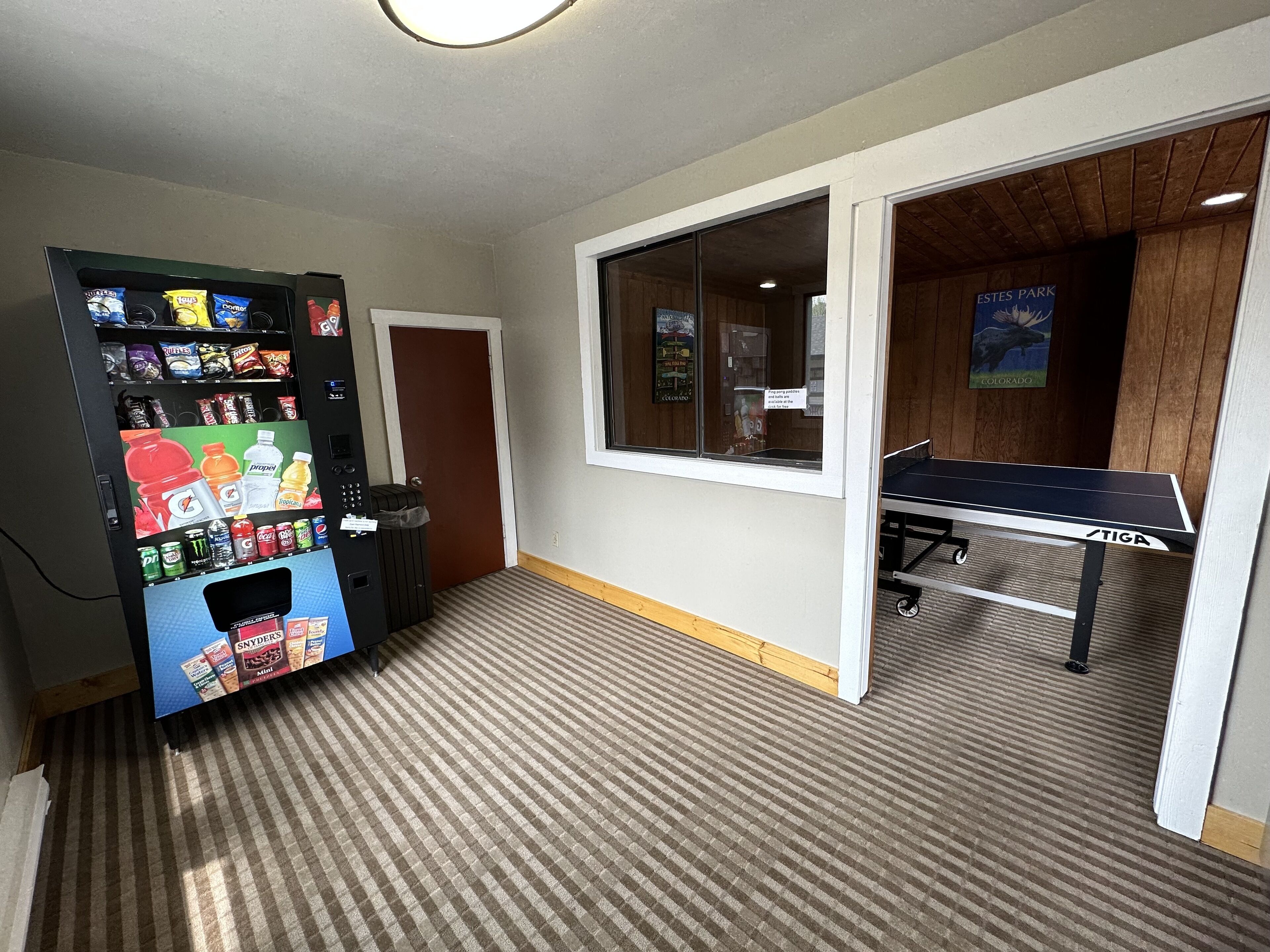 Een kamer met een automaat, een tafeltennistafel en een raam met een poster.
