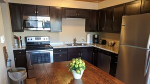 A kitchen with dark wooden cabinets, stainless steel appliances, and a wooden countertop with a bowl of green apples. - Estes Mountain Inn (Estes Park)