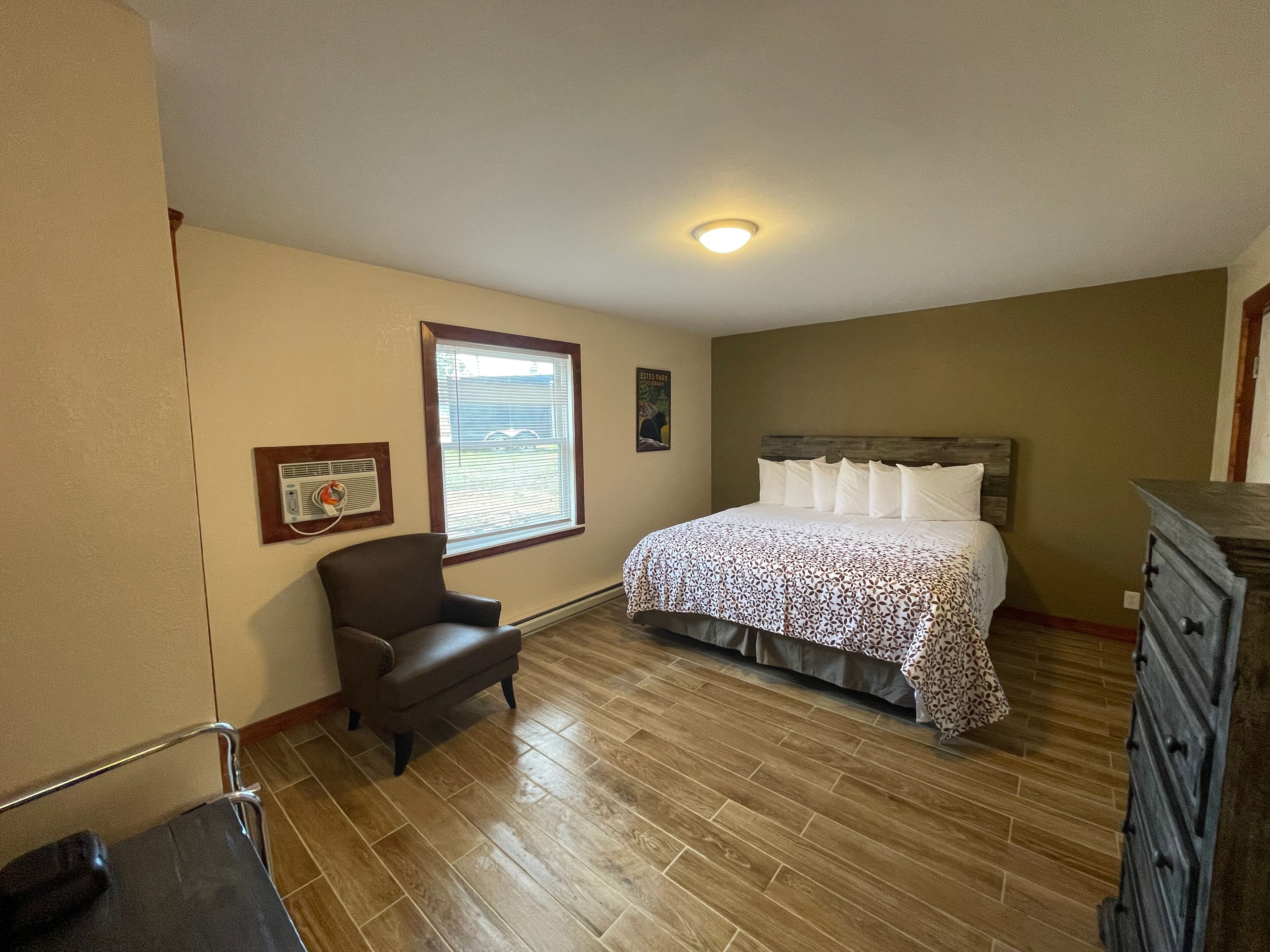 Quarto com cama, cadeira, cômoda, janela com persianas e luminária no teto.