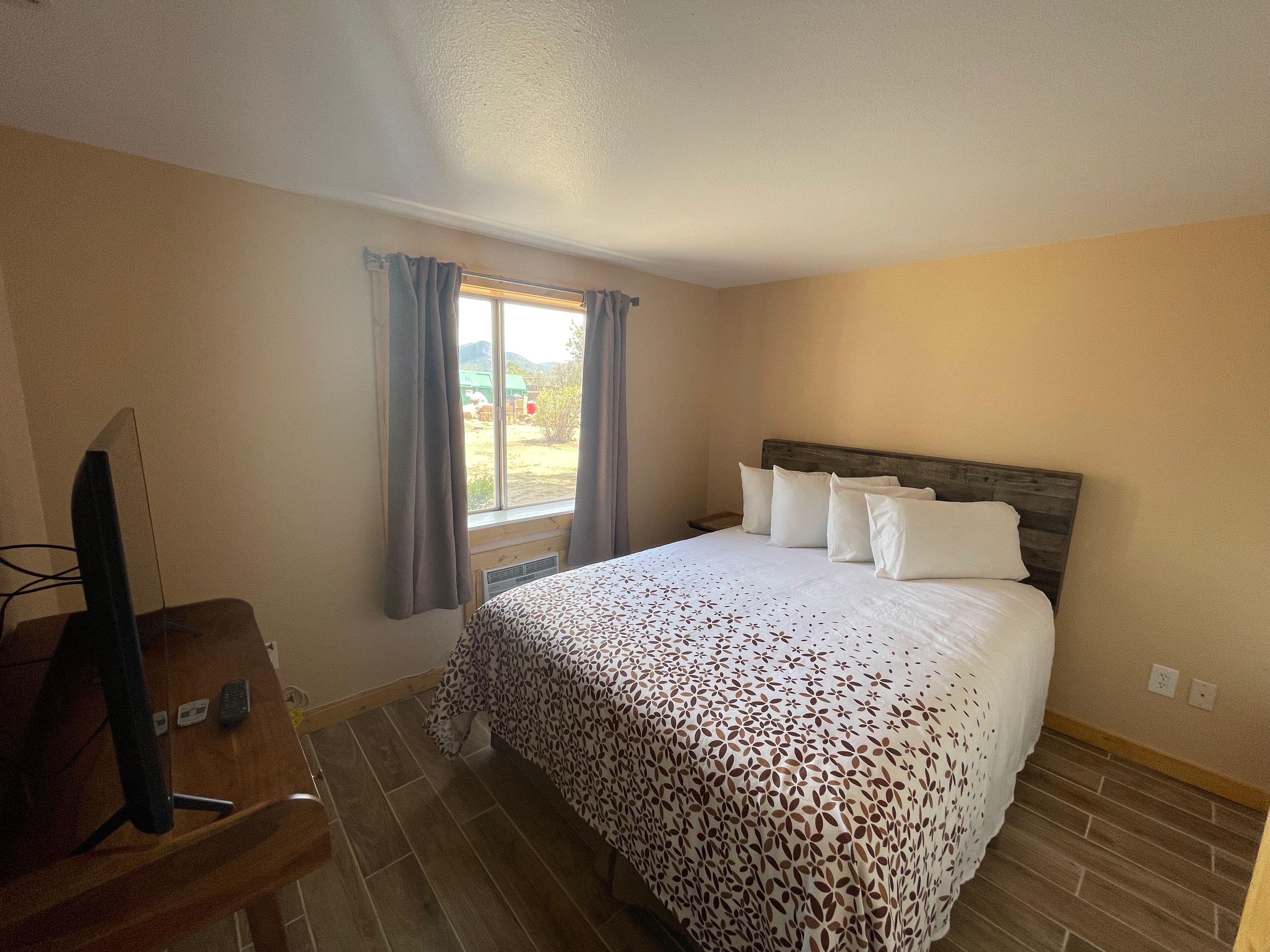 Una habitación de hotel con cama, un escritorio con silla, televisión y ventana con cortinas.
