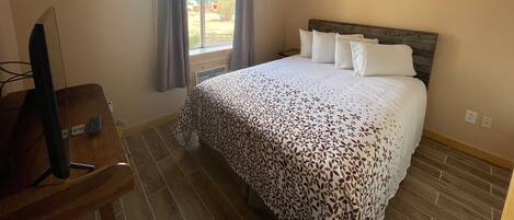 A hotel room with a bed, a desk with a chair, a television, and a window with curtains.